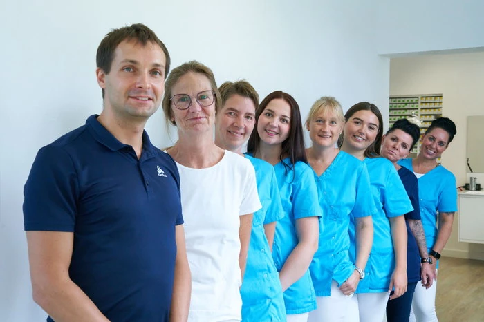 Team einer modernen Zahnarztpraxis steht freundlich lächelnd im Behandlungsraum.