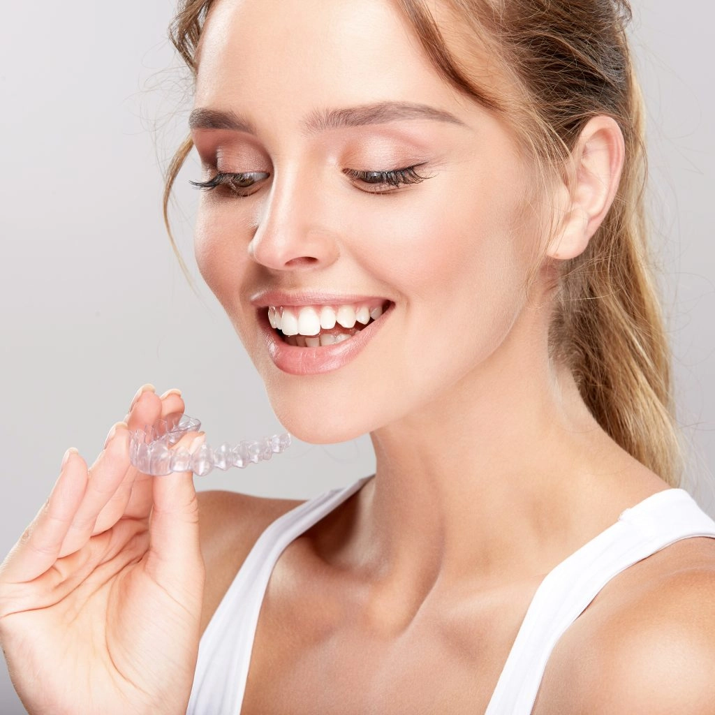 Junge Frau hält durchsichtige Zahnschiene und lächelt, Zahnkorrektur und Aligner.